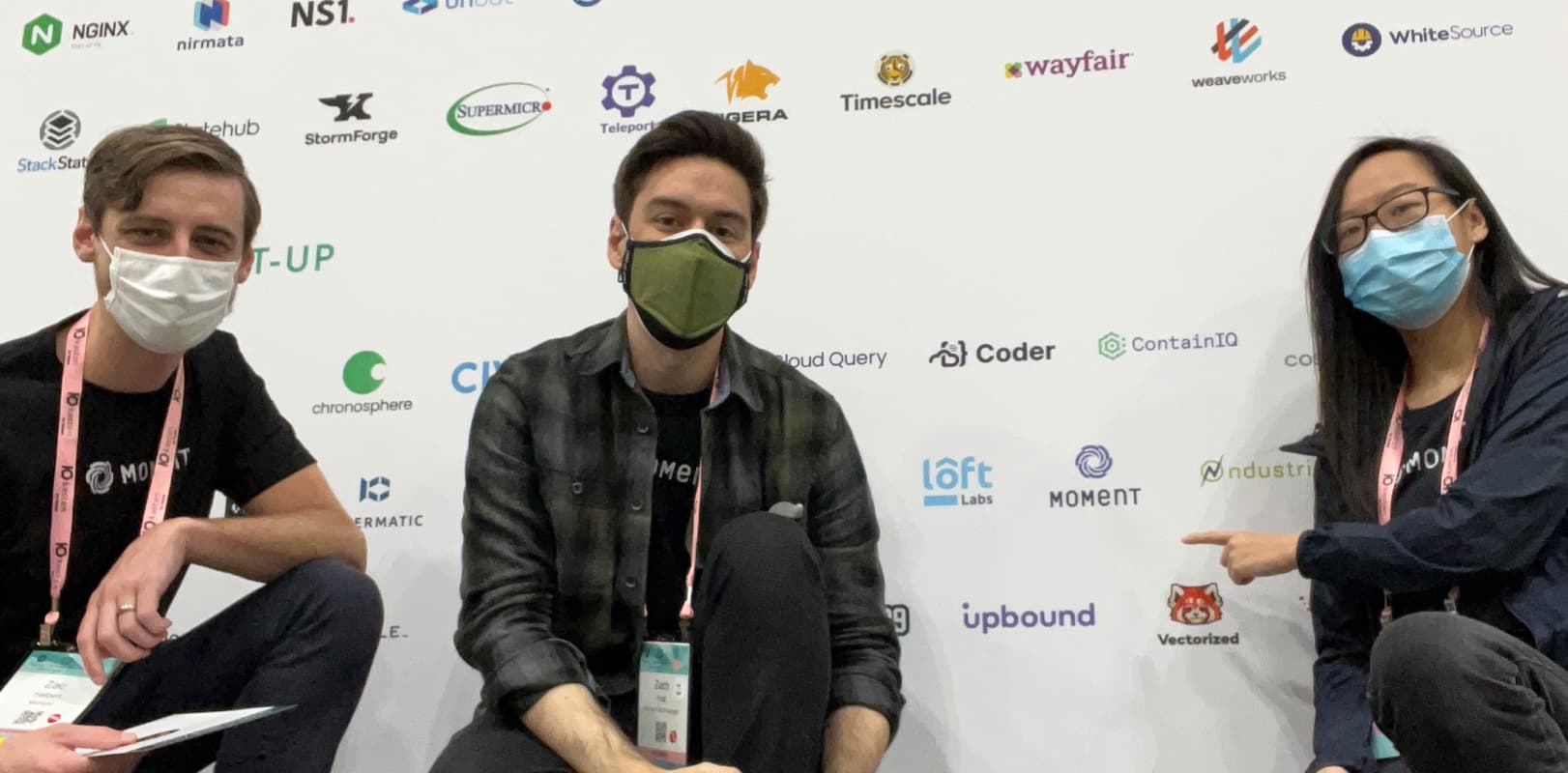 The Moment team shows off the Moment logo on the wall of sponsors at KubeCon 2021 in Los Angeles California